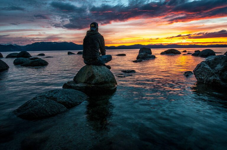 person on stone overlooking lake